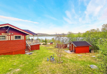 Cabaña roja junto al lago en Jarfjord, Suecia, rodeada de vegetación y una bicicleta en el jardín.