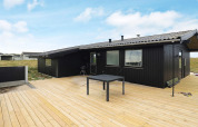 Casa de vacaciones negra con terraza de madera y jardín, Hjørring, Dinamarca, bajo cielo azul y soleado.