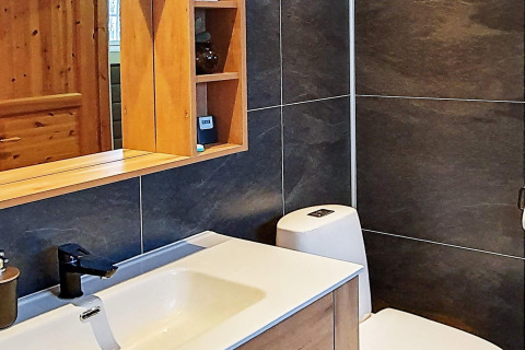 Bagno moderno in chalet svedese con rivestimenti scuri, lavabo, specchio, armadietto e rubinetto nero.