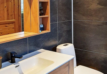 Modern bathroom in a Swedish chalet featuring wood cabinets, mirror, sink, black faucet, and dark tiles.
