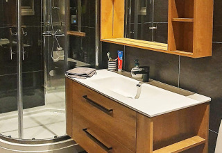 Baño moderno con armario de madera, espejo, ducha y lavabo en un chalet vacacional en Jarfjord, Suecia.
