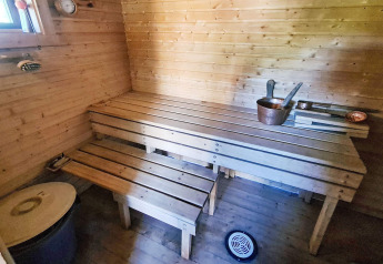 Indvendigt billede af en traditionel sauna med træbænke og kobberspand i et feriehus i Jarfjord, Sverige.