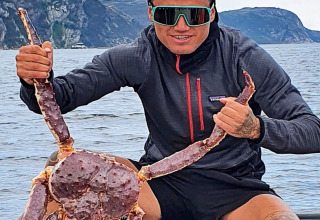 Man in donkere jas houdt grote krab vast bij water en bergen bij 7-persoons vakantiehuis in Jarfjord, Zweden.
