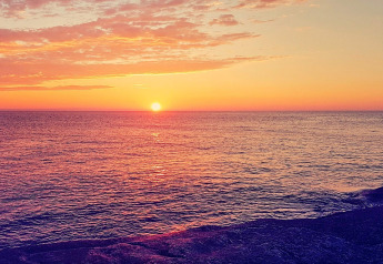 Sunset over the sea viewed from a chalet in Jarfjord, Sweden, with vivid clouds and calm ocean waves.