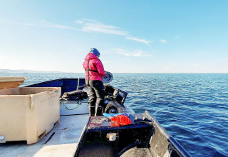 Persona con giacca rossa su una barca in Svezia, circondata da acqua blu e cielo sereno e limpido.
