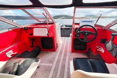 Cockpit van een rode motorboot met stuur en meerzicht bij Jarfjord, vakantiehuis in Zweden.