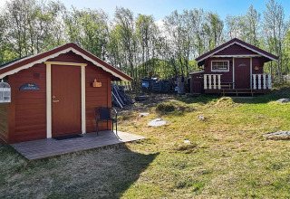 Zwei rote Holzhütten im Grünen beim Ferienhaus in Jarfjord, Schweden, umgeben von Bäumen.
