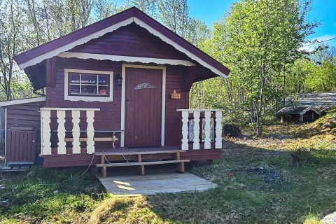 Rød og hvid bjælkehytte med terrasse i et frodigt, grønt område i Jarfjord, Sverige, under solskin.