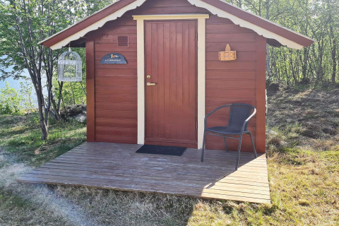 Rode houten chalet met veranda, stoel en vogelkooi, omgeven door bomen in Jarfjord, Zweden.