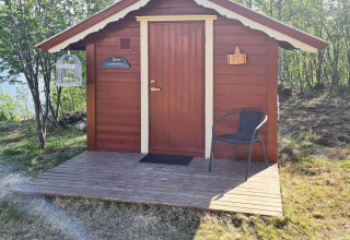 Chalet rouge en bois avec terrasse, chaise et cage à oiseaux, entouré d’arbres à Jarfjord en Suède.