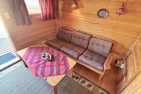 Salon chaleureux dans un chalet en bois avec canapé, table et rideaux rouges, Jarfjord, Suède.