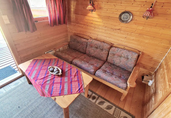 Hyggelig opholdsstue i træchalet med sofa, bord og røde gardiner, feriebolig i Jarfjord, Sverige.