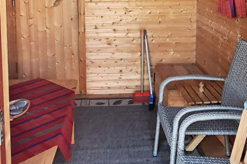 Foto interior de un chalet de madera con sillas de mimbre, mesa, utensilios de limpieza y alfombra.
