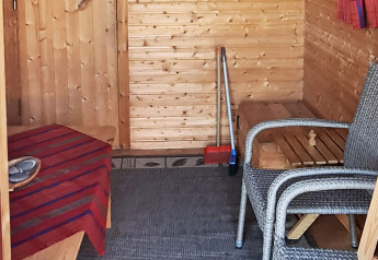 Binnenfoto van een houten chalet met rotan stoelen, tafel, schoonmaakgerief en een kleurrijk tapijt.