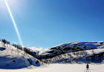 Person skiing in a snowy valley under clear blue sky near '7 person holiday home in JARFJORD', Sweden.