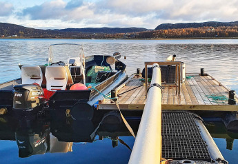 Bateau avec moteur Suzuki amarré à un ponton en bois, vue sur l'eau depuis un chalet à Jarfjord, Suède.
