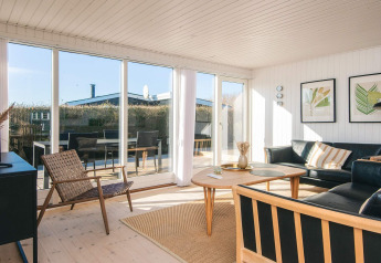 Salón luminoso en 'Renovated Beach House' en Dinamarca con grandes ventanales y decoración moderna.