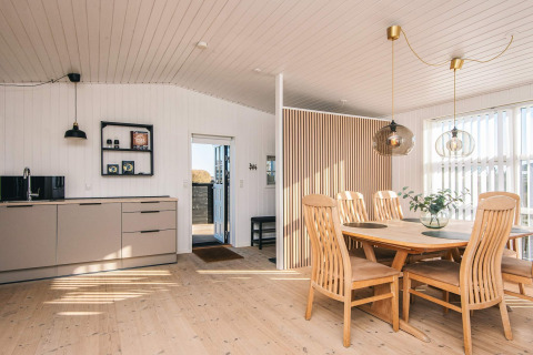 Casa de playa renovada en Dinamarca con cocina luminosa, mesa de comedor de madera y mucha luz natural.