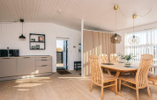 Casa de playa renovada en Dinamarca con cocina luminosa, mesa de comedor de madera y mucha luz natural.