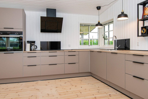 Moderne keuken in het Renovated Beach House in Denemarken met lichte kasten, houten blad en grote ramen.
