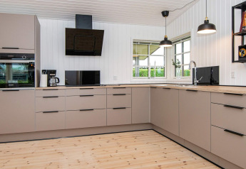 Cocina moderna en la Renovated Beach House de Dinamarca con gabinetes claros, madera y amplias ventanas.