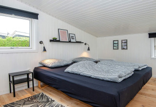 Chambre du 'Renovated Beach House' au Danemark avec lit noir, murs blancs et décoration moderne.