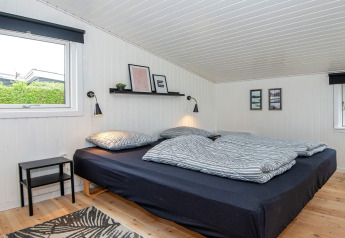 Dormitorio en 'Renovated Beach House' en Dinamarca con cama negra, paredes blancas y decoración moderna.