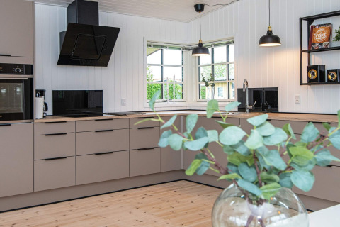 Cucina moderna presso il Renovated Beach House in Danimarca con mobili chiari, grandi finestre e dettagli in legno.