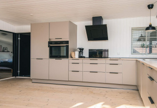 Moderne keuken in het gerenoveerde strandhuis in Denemarken met beige kasten en stijlvolle afwerking.