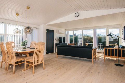 Sala luminosa y moderna en la Renovated Beach House en Dinamarca, con muebles de madera y grandes ventanales.