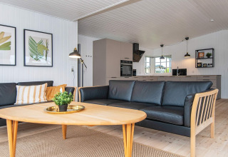 Lichte, moderne woonkamer in het Renovated Beach House in Denemarken met zwarte bank en open keuken.