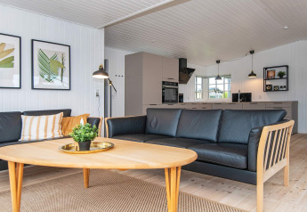 Salón moderno y luminoso en el Renovated Beach House de Dinamarca, con sofá negro y cocina abierta.