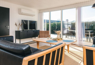 Acogedora sala de estar en Renovated Beach House en Dinamarca con ventanales y muebles modernos de madera.