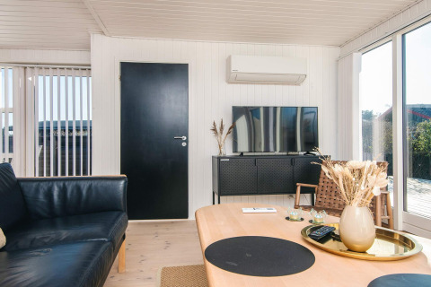 Soggiorno del Renovated Beach House in Danimarca con porta nera, TV, aria condizionata e decori naturali.