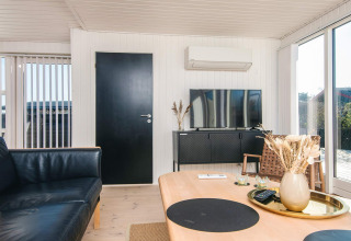 Woonkamer in het gerenoveerde strandhuis in Denemarken met zwarte deur, tv, airco en lichte inrichting.