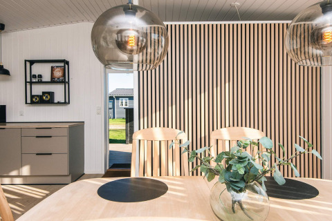 Eetgedeelte in het Renovated Beach House in Denemarken met houten lamellenwand en moderne hanglampen.