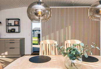 Comedor en el Renovated Beach House de Dinamarca con pared de listones, lámparas colgantes y decoración moderna.