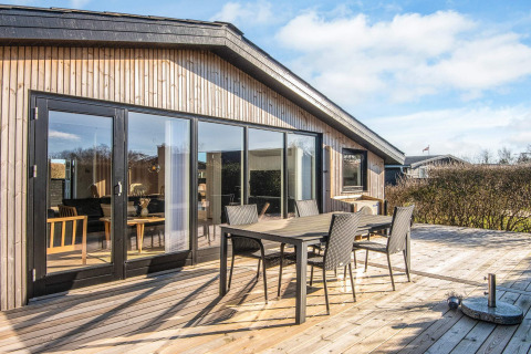 Sonnige Holzterrasse mit modernen Gartenmöbeln am renovierten Strandhaus in Dänemark.