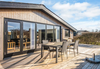 Terraza de madera soleada con modernos muebles de exterior en el Renovated Beach House en Dinamarca.