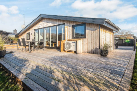 Zonnig houten terras bij het gerenoveerde strandhuis in Denemarken met buiteneethoek en grote ramen.
