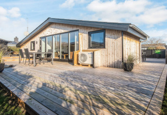 Terraza de madera soleada en el Renovated Beach House en Dinamarca, con comedor exterior y grandes ventanas.