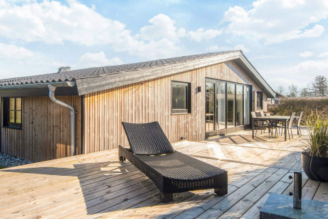 Solrig terrasse ved det renoverede strandhus i Danmark med liggestol, spisebord og moderne træfacade.