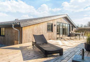 Zonnig terras bij het Renovated Beach House in Denemarken met ligstoel, eettafel en houten gevel.