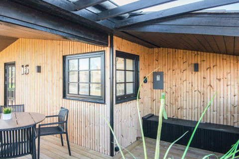 Udendørs terrasseområde på 'Renovated Beach House' i Danmark, med sort rammede vinduer og trævægge.