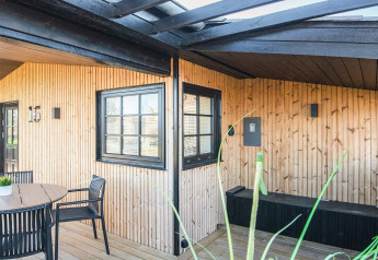Udendørs terrasseområde på 'Renovated Beach House' i Danmark, med sort rammede vinduer og trævægge.
