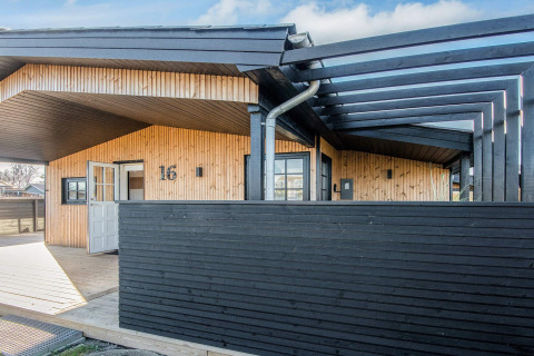 Renoviertes Strandhaus in Dänemark mit moderner Holzfassade, schwarzem Zaun und überdachtem Eingangsbereich.