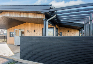 Casa de playa renovada en Dinamarca con valla de madera negra y entrada abierta bajo cubierta moderna.