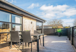 Terraza de madera soleada con muebles de exterior negros en la Renovated Beach House en Dinamarca.