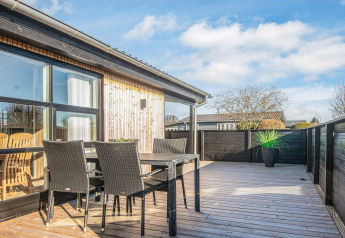 Terraza de madera soleada con muebles de exterior negros en la Renovated Beach House en Dinamarca.