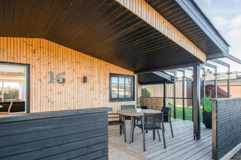 Maison de plage rénovée au Danemark avec terrasse en bois, toit noir, table extérieure et numéro 16.